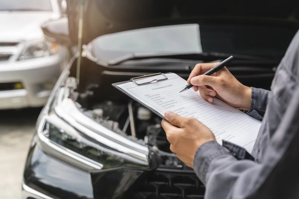 Mechanic writing up an inspection checklist beside an open bonnet